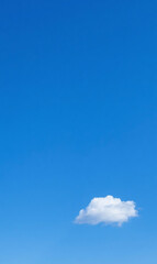 A solitary white cumulus cloud drifts across a vast, clear blue sky on a bright sunny day, embodying tranquility and minimalism