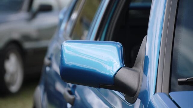 Blue metallic car rearview mirror closeup. Handheld shot of aesthetic exterior of youngtimer in parking lot.