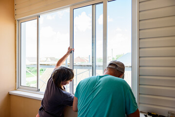 Masters repairing or installing metal-plastic window on a balcony in a house.