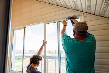 Masters repairing or installing metal-plastic window on a balcony in a house.
