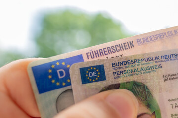 German ID card and driver’s license in hand, EU flag, Modern European driving permit,...