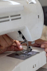 Detailed view of a person's hands guiding a thread through the needle of a modern white sewing machine. This captures the precise action involved in preparing to sew.