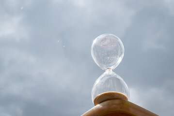 An hourglass sparkles in the sun against the sky. A glass hourglass with all the sand run out...