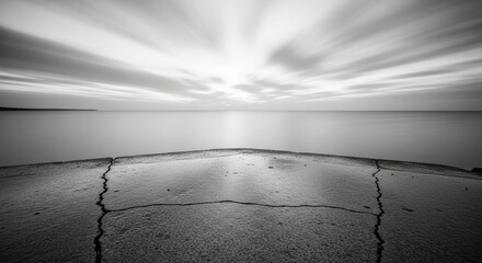 Dramatic black and white long exposure of cracked pier leading to calm ocean horizon