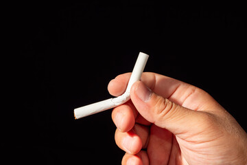 A single hand holds a bent and broken cigarette against a dark background, symbolizing the act of quitting smoking.