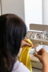 A woman's hands meticulously trim yellow fabric with small scissors near a sewing machine. This...