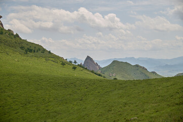 Rolling green hills under a vast cloudy sky leading to a distant rocky peak