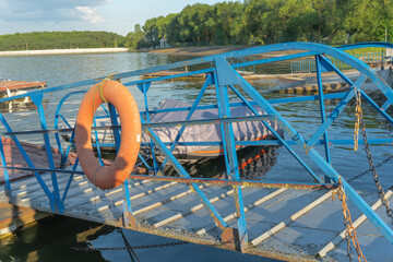 Rustic blue painted metal pier with lifebuoy tied on railing leading to peaceful river with moored...