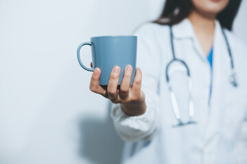 Portrait of Asian doctor woman standing holding coffee cup in white studio background