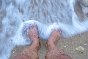 Sea waves gently washing over a man's feet while standing on the beach, enjoying the warm sand and soothing ocean breeze