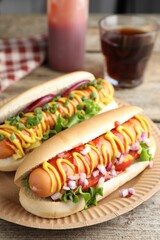 Delicious hot dogs with sauces, lettuce and onion on wooden table, closeup
