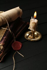 Old rolled scroll, burning candle and books on black wooden table, closeup