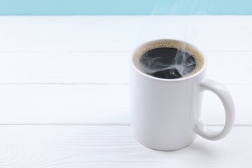 Aromatic coffee in cup on white wooden table against light blue background, closeup. Space for text