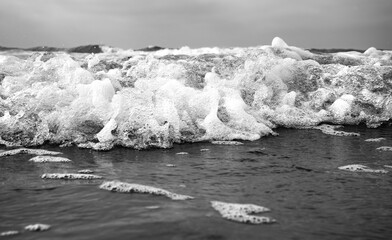 Breaking wave from worm's-eye view, rolling directly toward the camera. Contrasting black and white shot of surf with bubbles, foam and spray on the beach of Norderney in the Wadden Sea National Park
