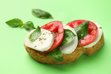 Delicious sandwich with mozzarella cheese, tomatoes and basil on green background, closeup