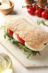Delicious sandwich with mozzarella cheese, tomatoes and arugula on light wooden table, closeup