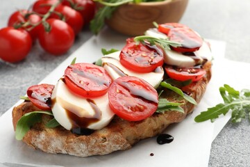 Delicious sandwich with mozzarella cheese, balsamic sauce, tomatoes and arugula on grey table, closeup