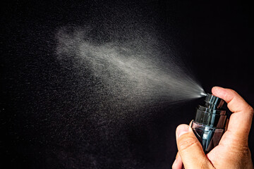 A hand holds a spray bottle, releasing a fine mist of liquid against a dark, contrasting background, capturing motion and texture.