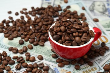 Roasted coffee beans, cup and dollar banknotes on white table, closeup