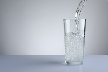 Pouring refreshing soda water into glass at white mirror table against light grey gradient...