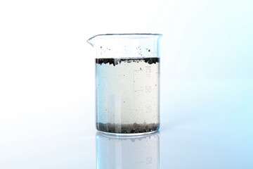 Glass beaker with dirty water on mirror surface