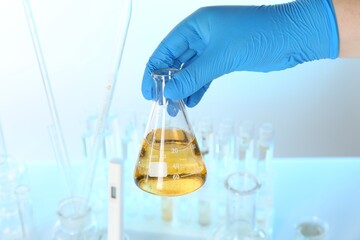Scientist holding flask with dirty water against blurred background, closeup