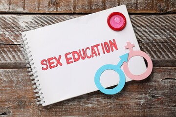 Notebook with phrase Sex Education, paper female and male gender symbols on wooden table, top view