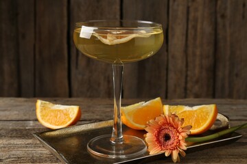 Martini cocktail in glass, orange slices and flower on wooden table, closeup