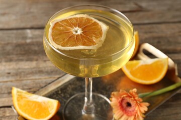 Martini cocktail in glass, orange slices and flower on wooden table, closeup
