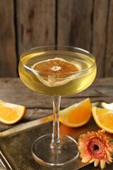 Martini cocktail in glass, orange slices and flower on wooden table, closeup