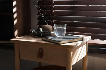 Wooden side table with glass of water, notebook and air reed diffuser indoors