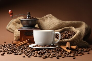 Cup of hot coffee, beans, grinder and cinnamon on brown background, closeup