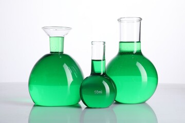 Different laboratory glassware with green liquid on mirror surface against white background