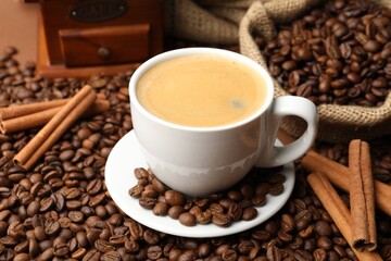 Cup of hot coffee, beans and cinnamon on brown background, closeup