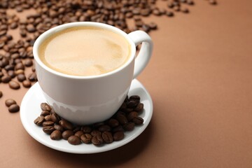 Cup of hot coffee and beans on brown background, closeup. Space for text