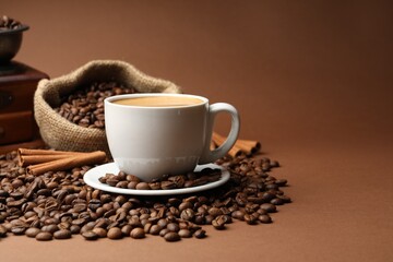 Cup of hot coffee, beans, grinder and cinnamon on brown background, closeup