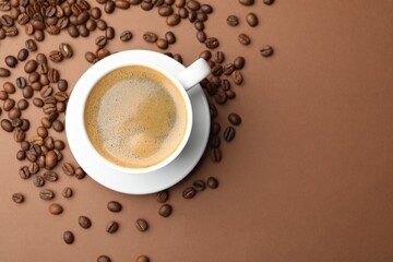 Cup of hot coffee and beans on brown background, flat lay. Space for text