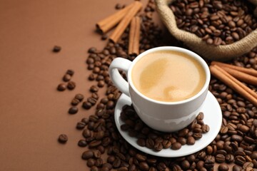 Cup of hot coffee, beans and cinnamon on brown background, closeup. Space for text