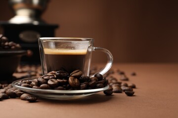 Cup of hot coffee, grinder and beans on brown background, closeup. Space for text