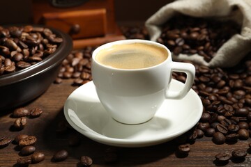 Aromatic coffee in cup and beans on wooden table, closeup