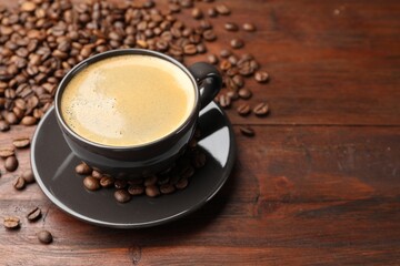 Aromatic coffee in cup and beans on wooden table, closeup. Space for text