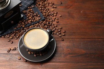 Aromatic coffee in cup, beans and grinder on wooden table, above view. Space for text