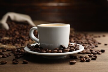 Aromatic coffee in cup and beans on wooden table, closeup