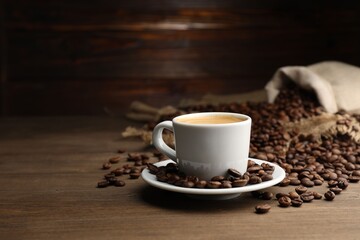 Aromatic coffee in cup and beans on wooden table, space for text
