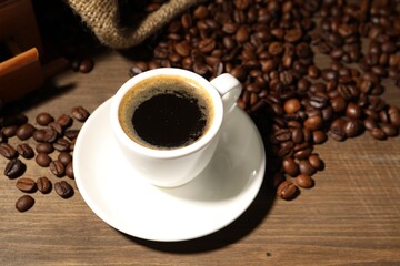 Aromatic coffee in cup and beans on wooden table, closeup