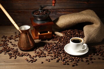 Aromatic coffee in cup, beans, cezve and grinder on wooden table