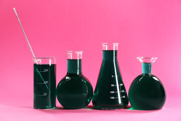 Laboratory glassware with green liquid on pink background