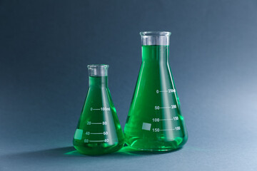 Laboratory glassware with green liquid on grey background