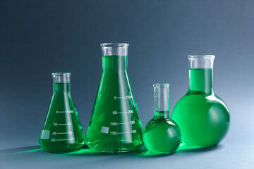 Laboratory glassware with green liquid on grey background