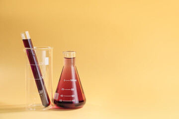 Laboratory glassware with colorful liquids on beige background. Space for text